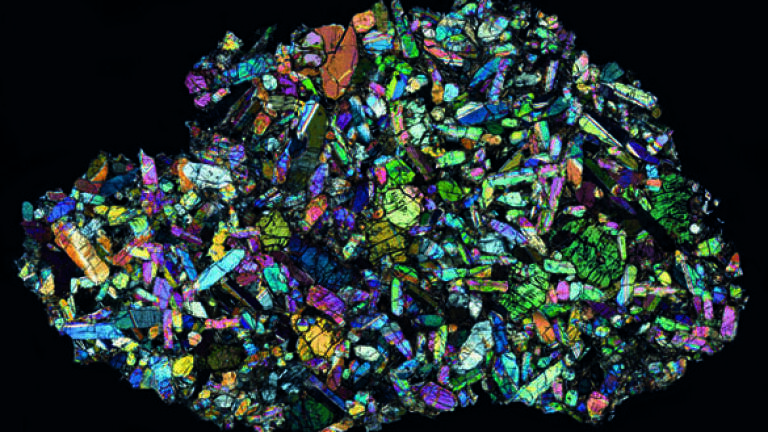A view of a thin section through a Martian meteorite found
at Nakhla, Egypt, in 1911. The sample is lit from below with
polarised light, then another polarising filter is placed between
the sample and the eyepiece. Different minerals rotate polarised
light by different amounts creating characteristic colours, so the
technique allows scientists to determine the minerals present.
This rock is a clinopyroxinite consisting largely of augite and
olivine with smaller amounts of other minerals. It is thought that
this rock formed around 1.38 billion years ago on Mars. It was
blasted from the surface of the planet by a huge impact event,
meandering its way through the Solar System for an unknown
time before hitting the Earth’s atmosphere and breaking up.
This sample is approximately 13mm across. Credit:© Natural History Museum London BM1913,
2642 and the Open University Virtual
microscope