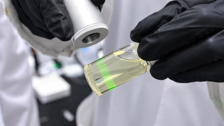 When a near-infrared laser is shined on these nanoparticles suspended in a liquid, they upconvert the light energy into bright green luminescence. Credit: Tyler Irving / University of Toronto Engineering